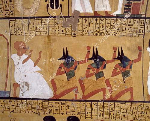 Pintado en la pared izquierda de la cámara funeraria de la tumba de Inherkau. El difunto, caracterizado por su cabeza rapada en señal de luto, está arrodillado ante tres sacerdotes que llevan una máscara con la cabeza de chacal del dios Anubis.