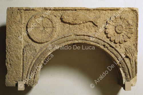 Arco in pietra decorato a rilievo con fiore palmette e pesce
